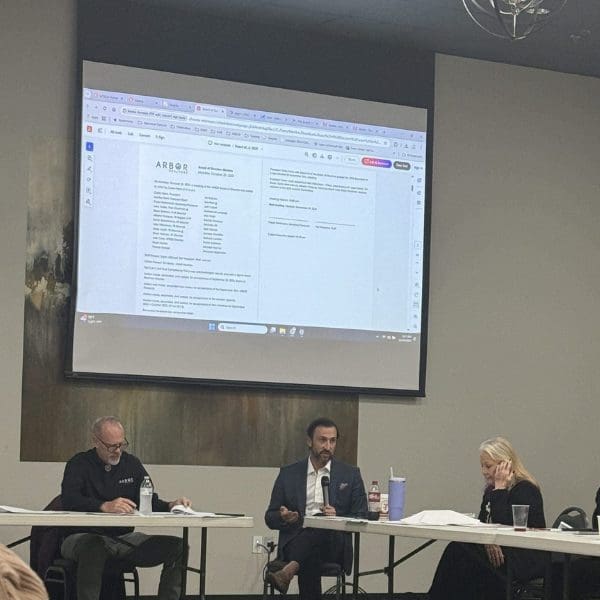 man sitting addressing a group with another man and a woman sitting on each side of him.